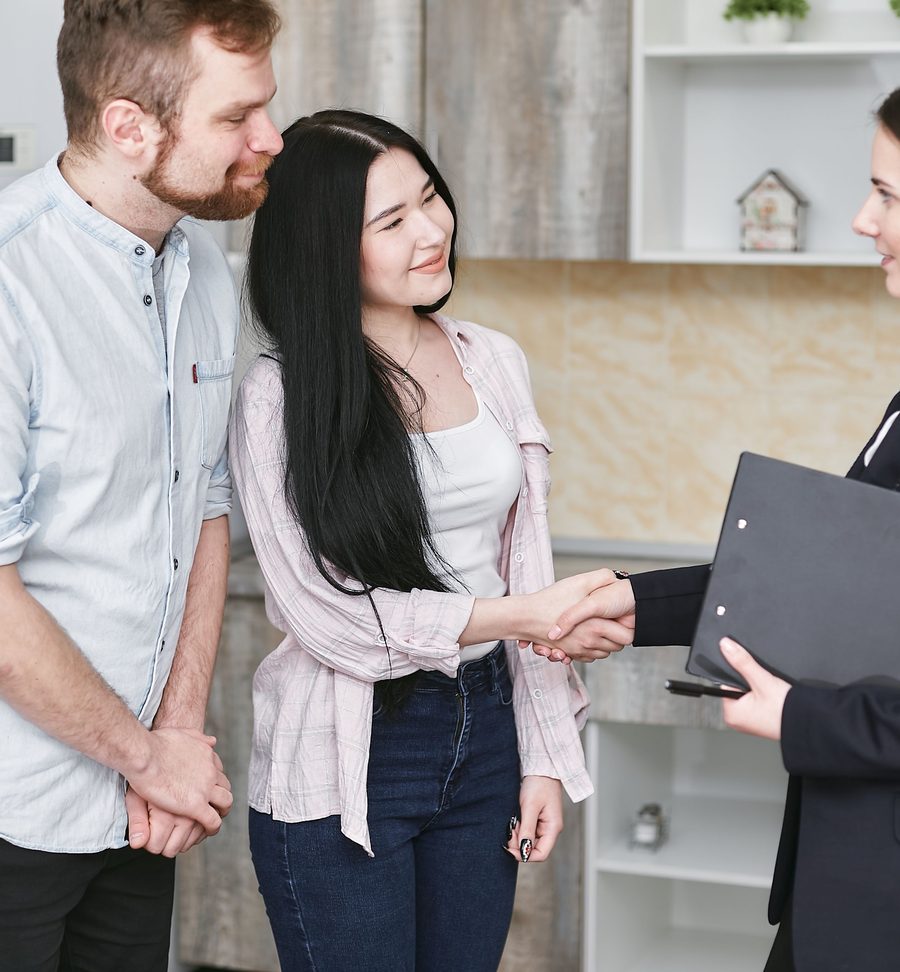 A homeowner smiling as she shakes hands with her plumber in the kitchen